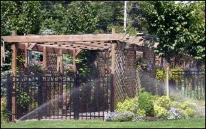Sprinklers running along a wooden pergola and iron fence garden